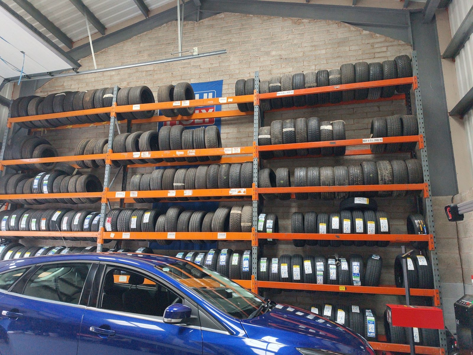 Inside Khan Motors: orange racking stacked with tyres along the whole wall, a blue car parked in front