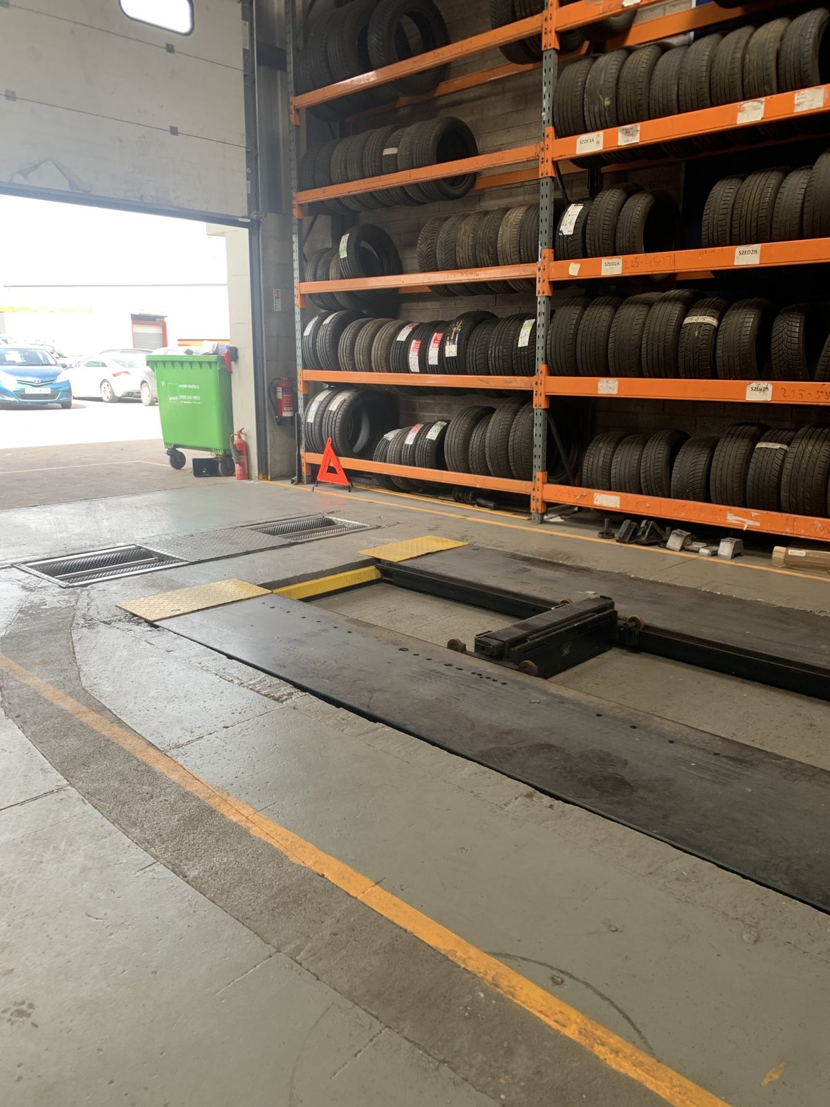 The MOT bay at Khan Motors, with the inspection lane in the floor and the roller door open to the yard