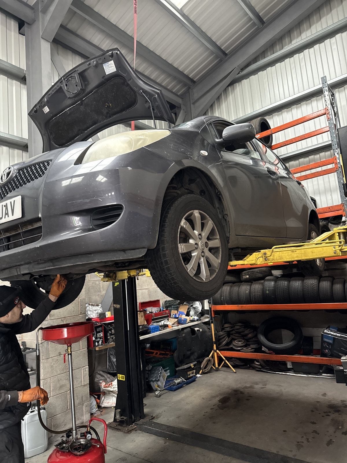 A grey car raised on the lift at Khan Motors with a mechanic working underneath